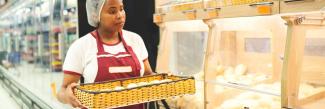 African American woman with tray of bread working at bakery.